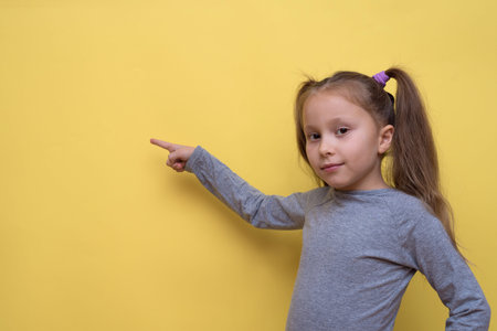 A cute girl in a gray T-shirt shows emotions on a yellow background.の写真素材