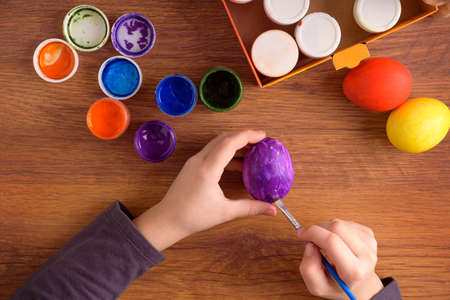 The child paints an egg for Easter. Set of paints on wooden backgroundの写真素材