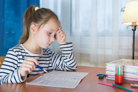 Dreamy little girl sit at desk studying look in distance visualizing or thinking, small child dreamer feel unmotivated distracted from preparing doing homework at home, lost in dreams or imaginationの写真素材