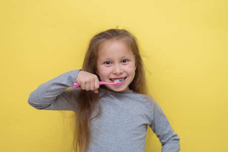 Charming little girl in t-shirt cleaning teeth with colorful kids toothbrush looking at cameraの写真素材