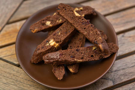 homemade chocolate biscotti with nuts and raisins on a brown plate on a tableの写真素材