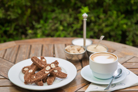 a plate of homemade chocolate biscotti cookies and a Cup of coffee with cream and sugar on the table. Blurred background