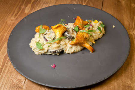 Risotto with wild mushrooms. On a black plate. On a rustic wooden backgroundの写真素材