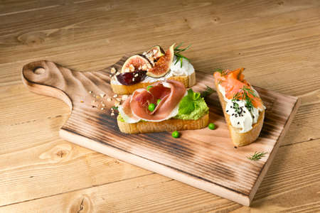 Tapas-assorted with salmon, jamon and figs. On a wooden Board. On a rustic wooden backgroundの写真素材