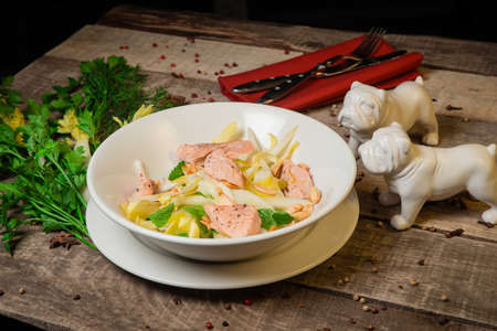 Warm salad with salmon, cheese and fresh herbs .On a white plate. On a rustic wooden backgroundの写真素材