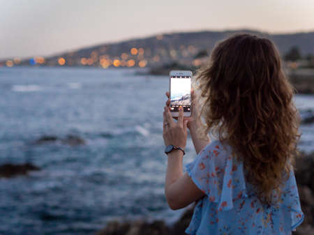 girl taking a photo of sunset on phone on the beach in Saint-Aygulf, France. Sunny day, clear skyの写真素材