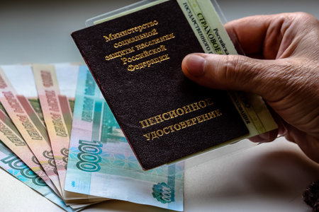 Woman's hand holding russian pension certificate, russian rubles in background. Russian translation - Ministry of Social Protection of Population of Russian Federation. Pension Certificate.の写真素材