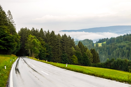 Beautiful mountain road in Austria. Misty forest and cloudy sky in background.の写真素材