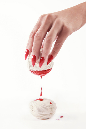Beautiful female hand with red manicure holding a marshmallow, with a dripping red paint on the marshmallows. White background. Nail extension. Manicure, Spa salon. Creative, advertising. Relax.の写真素材