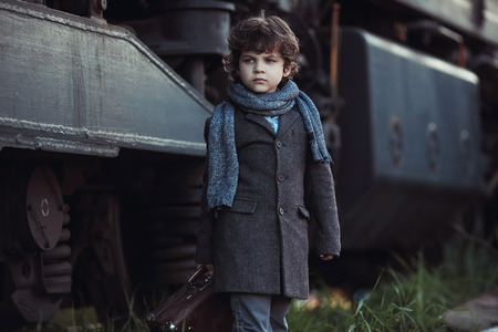 A little boy in a coat goes next to the train. Little traveler. Tourism. Vintage. Escape from home.の写真素材