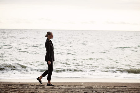 A beautiful young girl in a black suit, retro-image with a preceding, walks on the beachの写真素材
