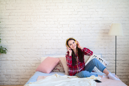 Portrait of beautiful woman in morning listening music sitting on bed at homeの写真素材