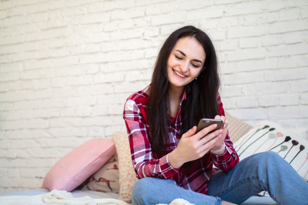 Young girl sitting on the bed and watching content on smart phoneの写真素材