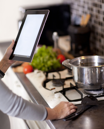 female hands holding a laptop at the dining table in the kitchenの写真素材