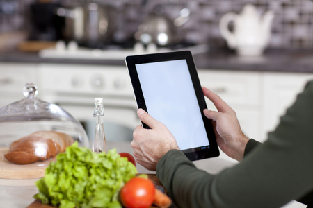 male hands holding a laptop at the dining table in the kitchenの写真素材