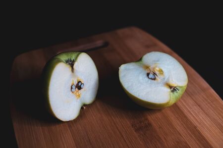 Sliced green apple is lying on a wooden Board. Organic fruit. Healthy lifestyle. Sweet fruit. Vegetarian healthy food. Natural background. Dark background.の写真素材