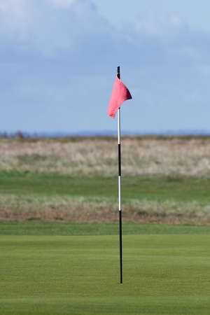 Red golf flag with blue skies in the backgroundの写真素材