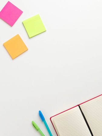 Top view of an open blank red notebook in the bottom corner with a green pen and a blue pen beside...