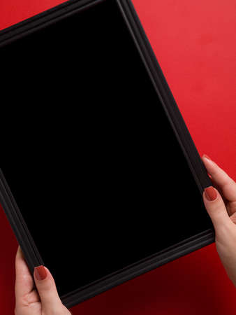 Top view of female hands holding a black empty frame in a red background with space for textの写真素材