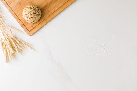 Top view of a marble table with a bread resting in a wooden board, wheat and flour with space for...