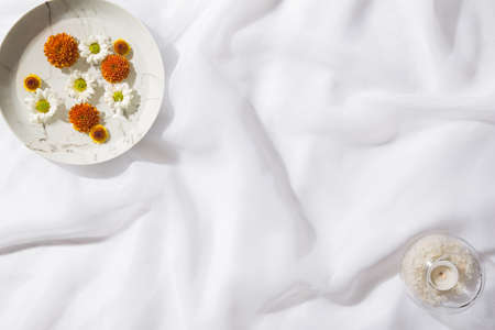 Top view of voile fabric background with a plate with floating flowers and a glass bowl with a candle and white rocks inside. Space for text.の写真素材