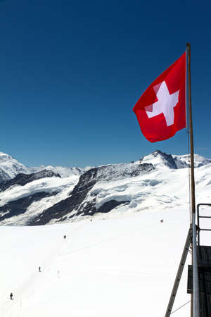 Swiss flag on top of mountains covered in snowの写真素材