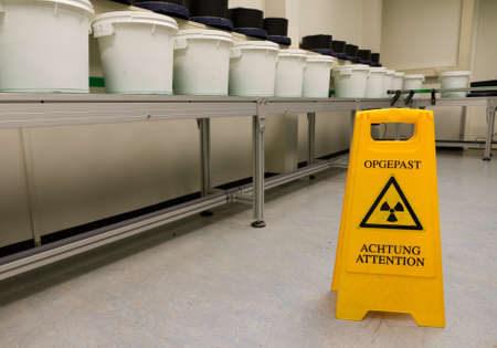 A sign warning for radioactivity on the ground next to a conveyor belt with buckets for transport on itの写真素材