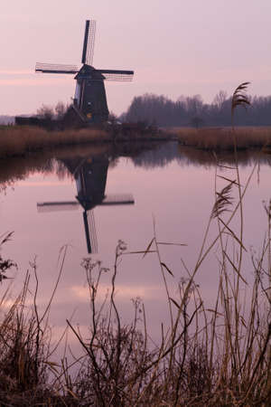 Old dutch mill reflected in the water at sunsetの写真素材