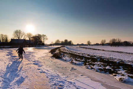 Ice skating in a beautiful snowy landscape at sunset in the Netherlandsの写真素材