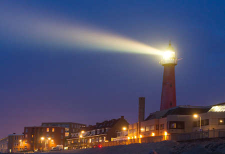 Lighthouse shines a beam of bright light towards the sea at twilight in Scheveningen, Netherlandsのeditorial素材
