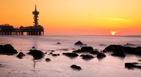 Sunset at Scheveningen, the Netherlands  Setting sun, rocks, the pier and silky smooth waterの写真素材