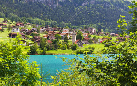 Look through some trees at a lake in Switzerland in the mountains with a little village on the shoreの写真素材