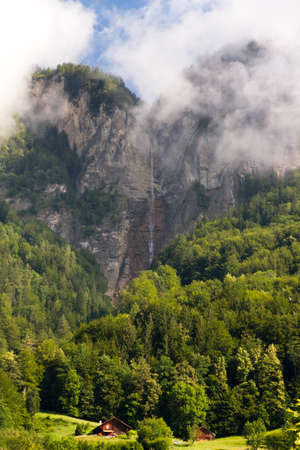 Beautiful swiss landscape with a waterfall, clouds and a small cabinの写真素材