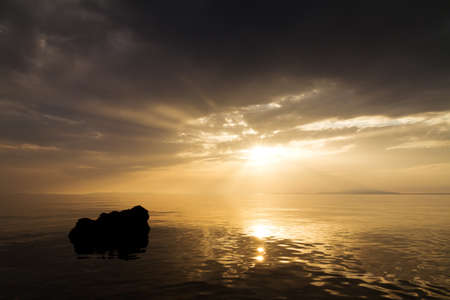 Beautiful sunset with clouds, a calm sea and a rockの写真素材