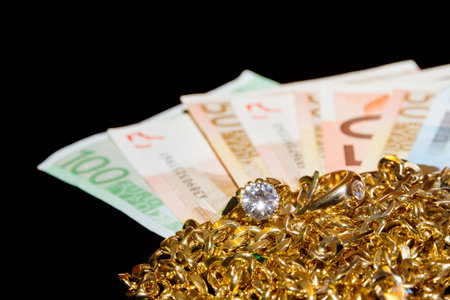 Money and gold jewellery against a black background