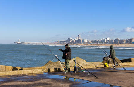 Fishermen on a jetty in Scheveningen, The Netherlands, with Scheveningen in the backgroundの写真素材
