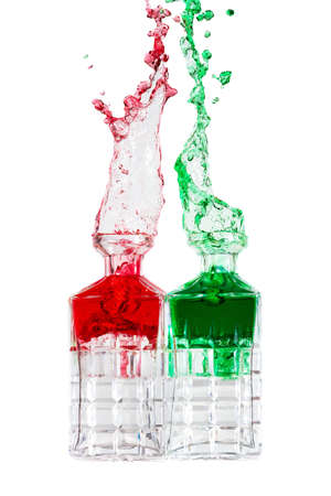 Crystal bottles splashing red and green liquid against a white backgroundの写真素材