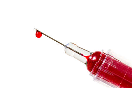 Close up image of a drop of red liquid on the needle of a syringe against a white backgroundの写真素材