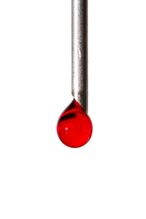 Close up image of a drop of red liquid on the needle of a syringe against a white backgroundの写真素材