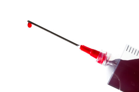 Close up image of a drop of red liquid on the needle of a syringe against a white backgroundの写真素材