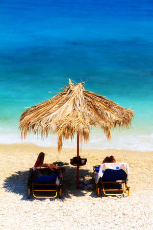 People are relaxing under a straw parasol on the beach at Xigia on the island of Zakynthosの写真素材