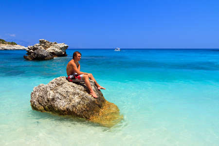 Handsome young man sits on a rock in the sea in summer on the greek island Zakynthosの写真素材