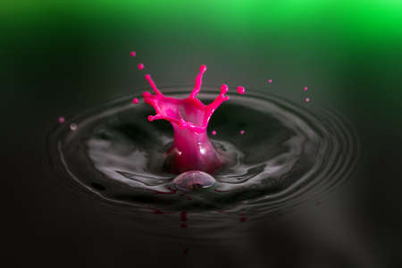Beautiful image of a drop of pink cream falling into green waterの写真素材