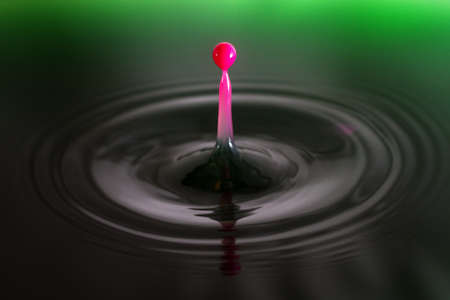 Beautiful image of a drop of pink cream falling into green waterの写真素材
