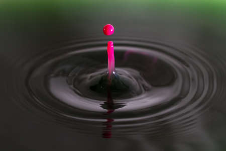 Beautiful image of a drop of pink cream falling into green waterの写真素材