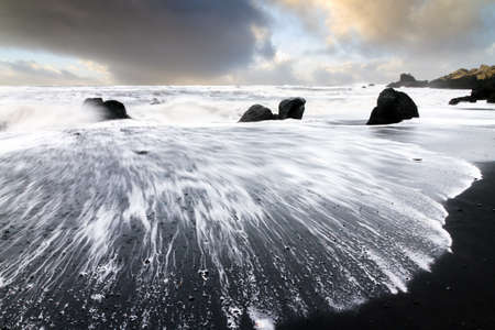 Beautiful sunset view of the black sand and rough sea at the beach of Vik in Icelandの写真素材