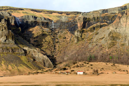 Beautiful typical farm at the bottom of the hill with waterfalls in Icelandの写真素材