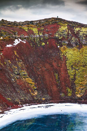 Tourist on top of the volcanic Kerid crater with the lake below, in Iceland in winterの写真素材