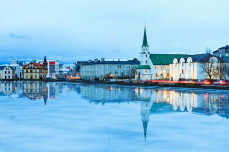 Beautiful reflection of the cityscape of Reykjavik and the Free church in lake Tjornin at the blue hour in winterの写真素材