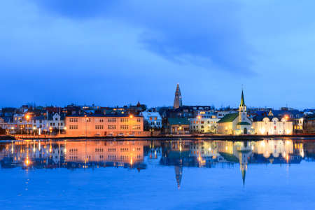 Beautiful reflection of the cityscape of Reykjavik in lake Tjornin at the blue hour in winterの写真素材